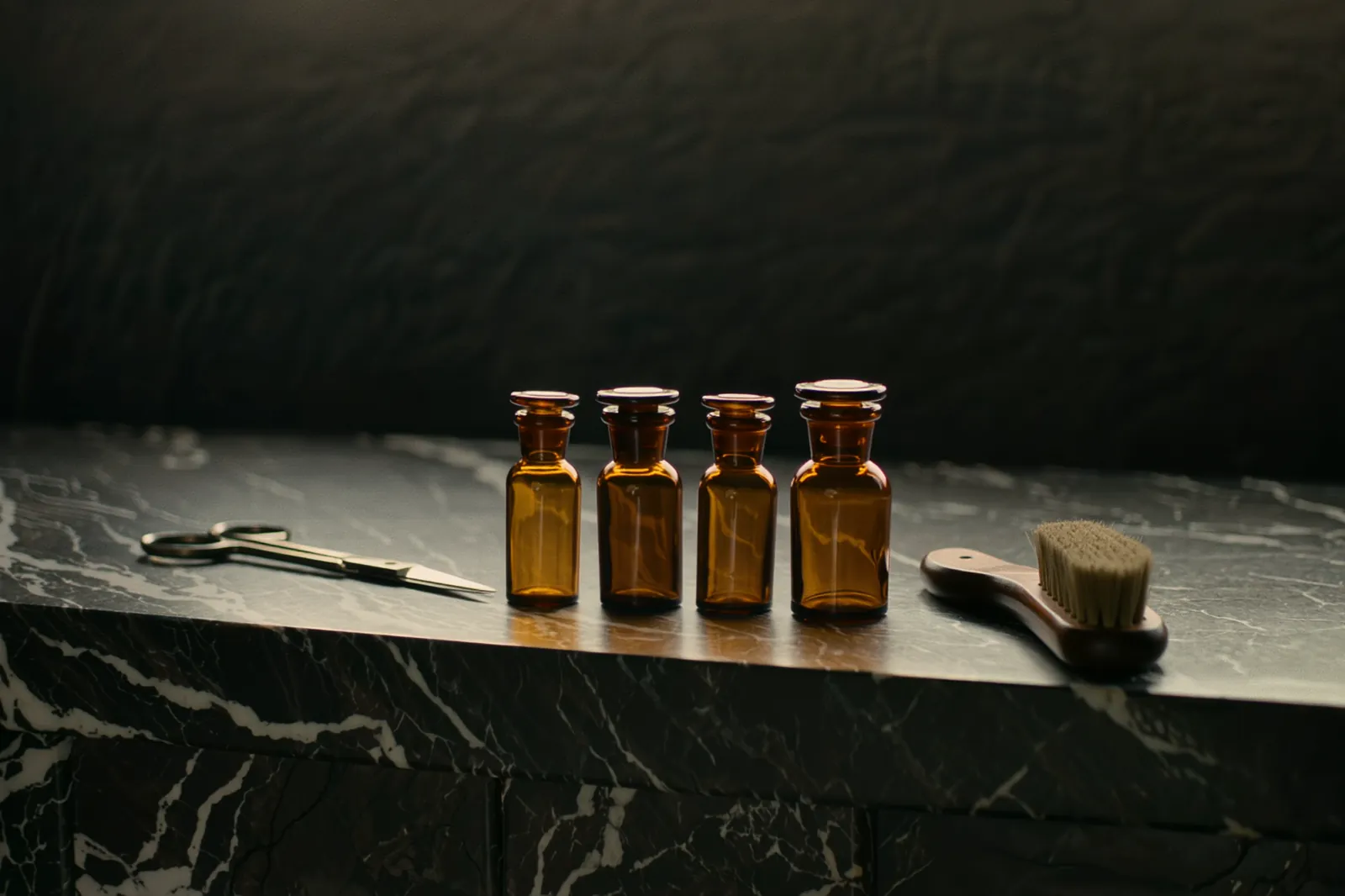 Amber and smoked-glass bottles, shears, and a horsehair brush on a black marble ledge.